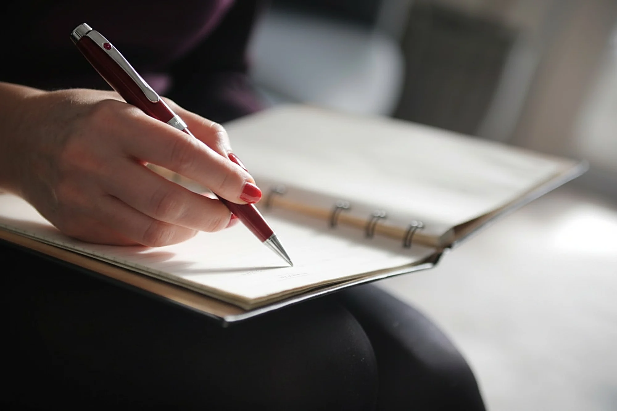 A hand taking notes in a notebook with an elegant pen in a calm, warm office